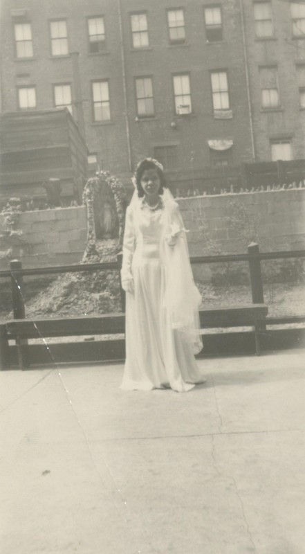 A bride in her wedding gown in front of a Virgin Mary statue and a building