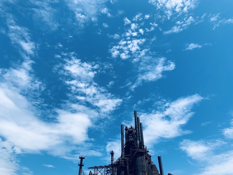 A steel mill against a blue sky. Its smoke stacks dominate the lower half of the image.