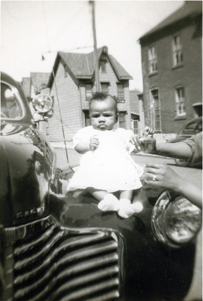 Little girl in a white dress sitting on the car's hood.