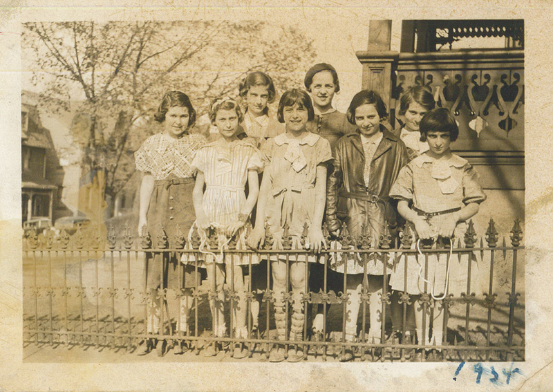 Several girls and women standing in front of a fence in two rows.
