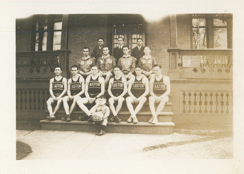Six young men wearing Easton basketball jerseys sitting on stairs. A small boy in front of them is holding a basketball with "1928-29" written on it.