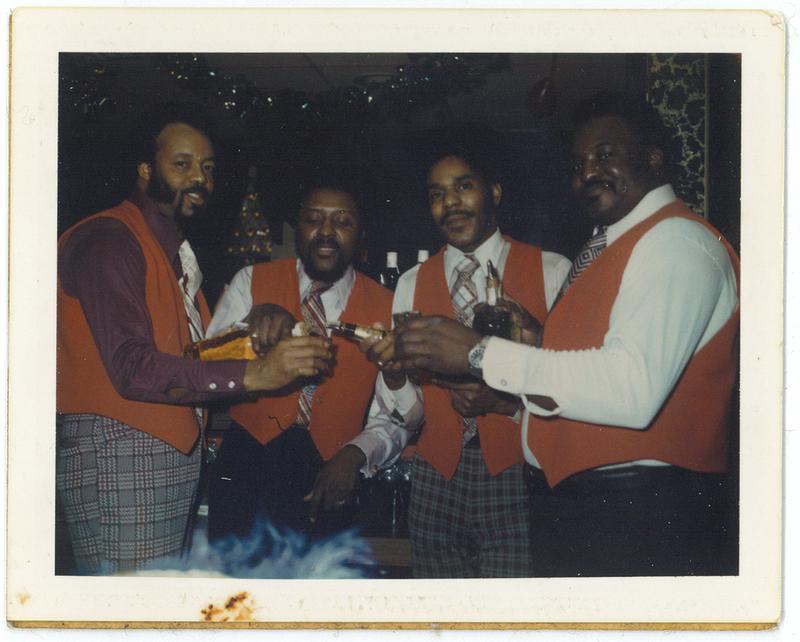 Four men wearing red vests with drinks in hand.