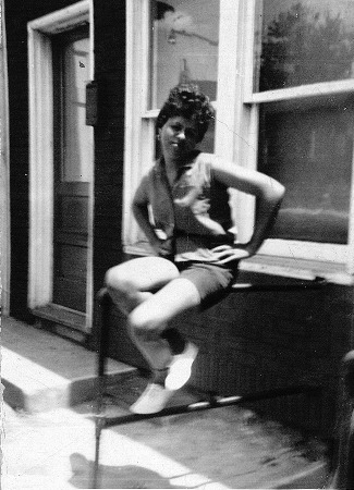 A woman in casual attire sitting on the railing in front of a house.