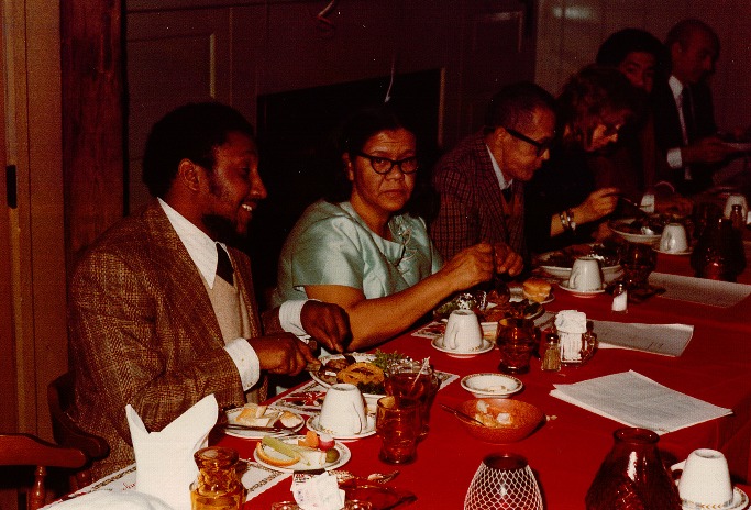 A group of men and women in holiday dresses sit and eat at the festive table.
