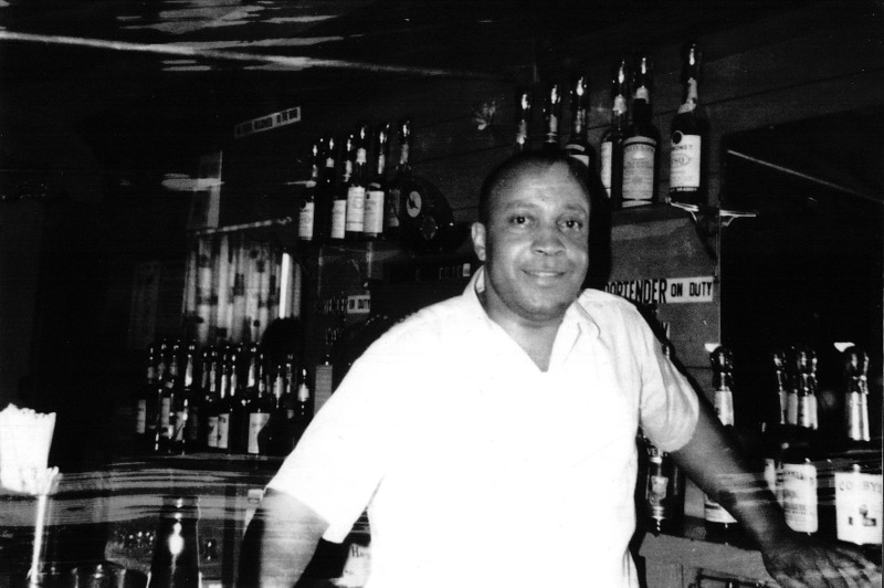 A man wearing white shirt stand in front of a bar counter.