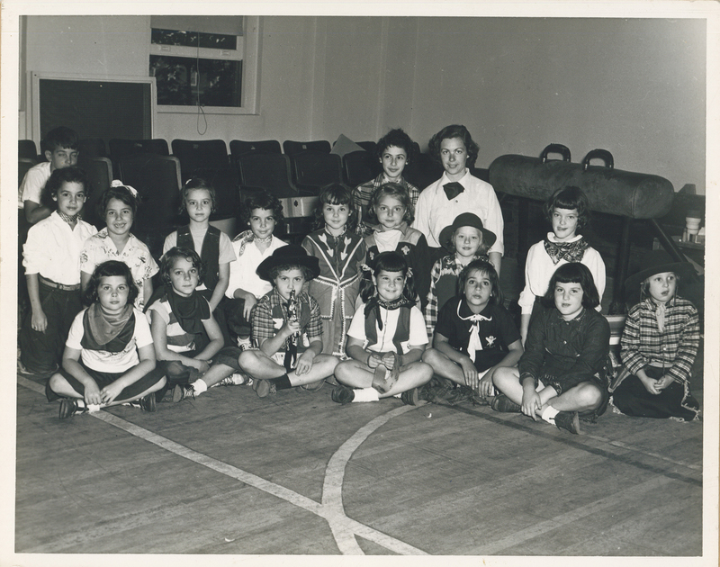 Several girls dressed as cowboys sitting cross-legged.