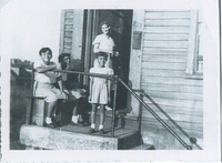Three children at the top of a stoop. A woman is standing in the house's doorway.