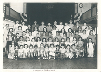 Several children sitting or standing in rows. They are flanked by camp counselors.
