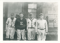 Four men standing next to each other in front of a house. They are all wearing Easton baseball uniforms.
