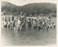 Several children and adults standing in a pool. Some children are holding hands above water.