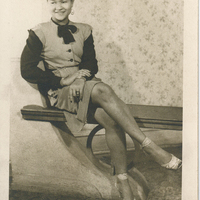 A woman in formal wear sitting on a bench. Her right leg is crossed over her left.