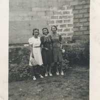 Three women in formal wear standing in front of a brick wall.