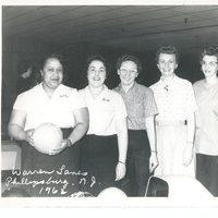 Five women standing in a row. The leftmost individual is holding a ball.