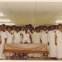 A group of women in white dresses standing in church in front of the table.