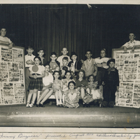 Several children flanked on either side by two individuals holding bulletin boards.