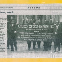 Newspaper clipping featuring a group of men in formal attires walking along the road and holding a poster.
