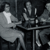 Two women and a man in formal wear sitting at a table.