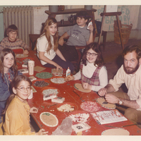 Several children seated at a table. There are various arts and crafts supplies on the table.